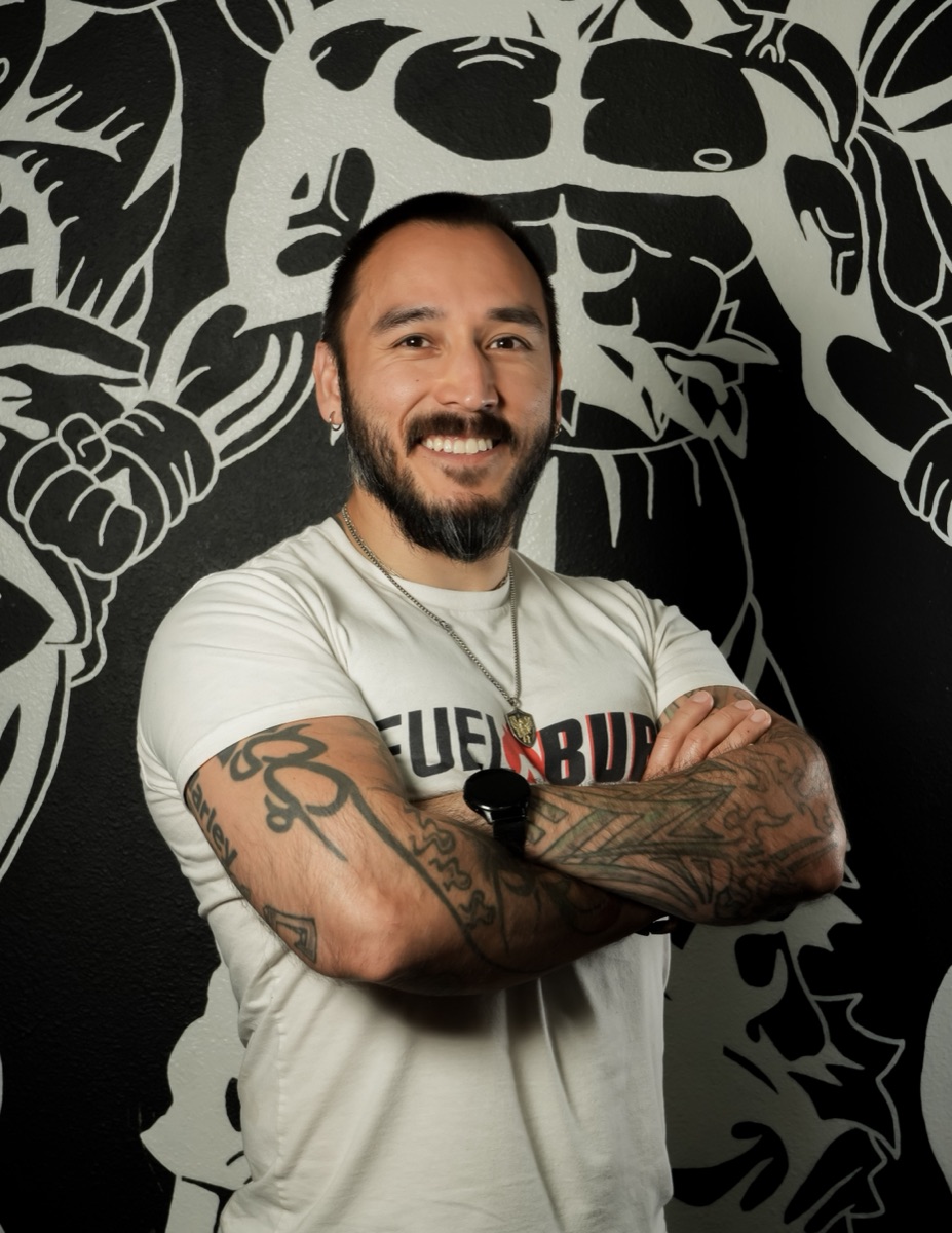 A personal trainer with crossed arms in front of a gym mural